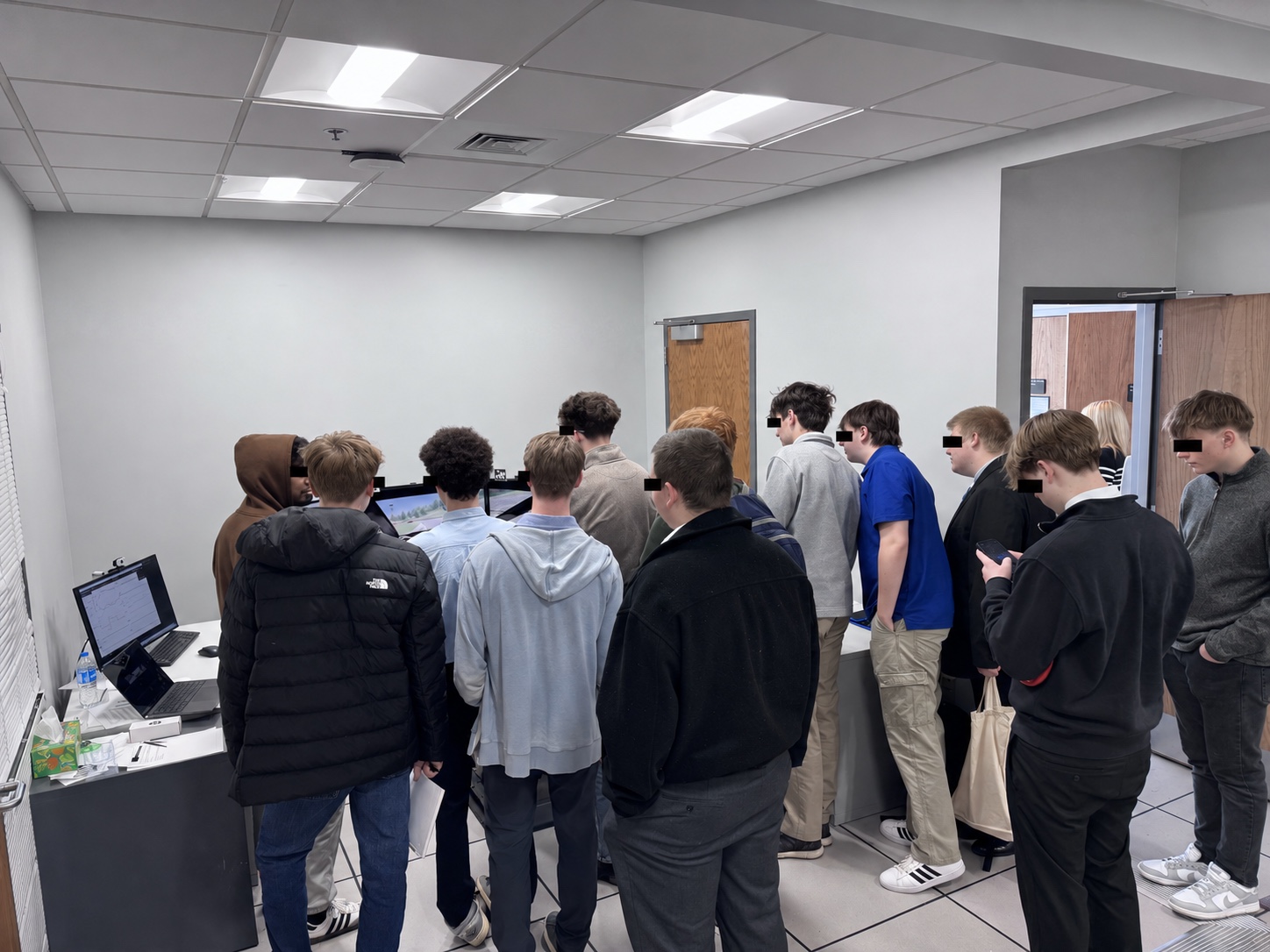 Ignite Institute students gather around the MINDxAI Lab driving simulator during their February 26, 2026 campus visit, with visible eyes covered for privacy.